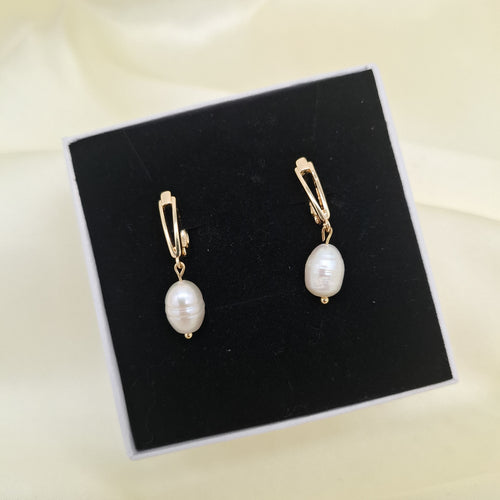 freshwater pearl drop earrings with gold-tone huggie hoop clasps, displayed on a black velvet jewelry box against a cream fabric background